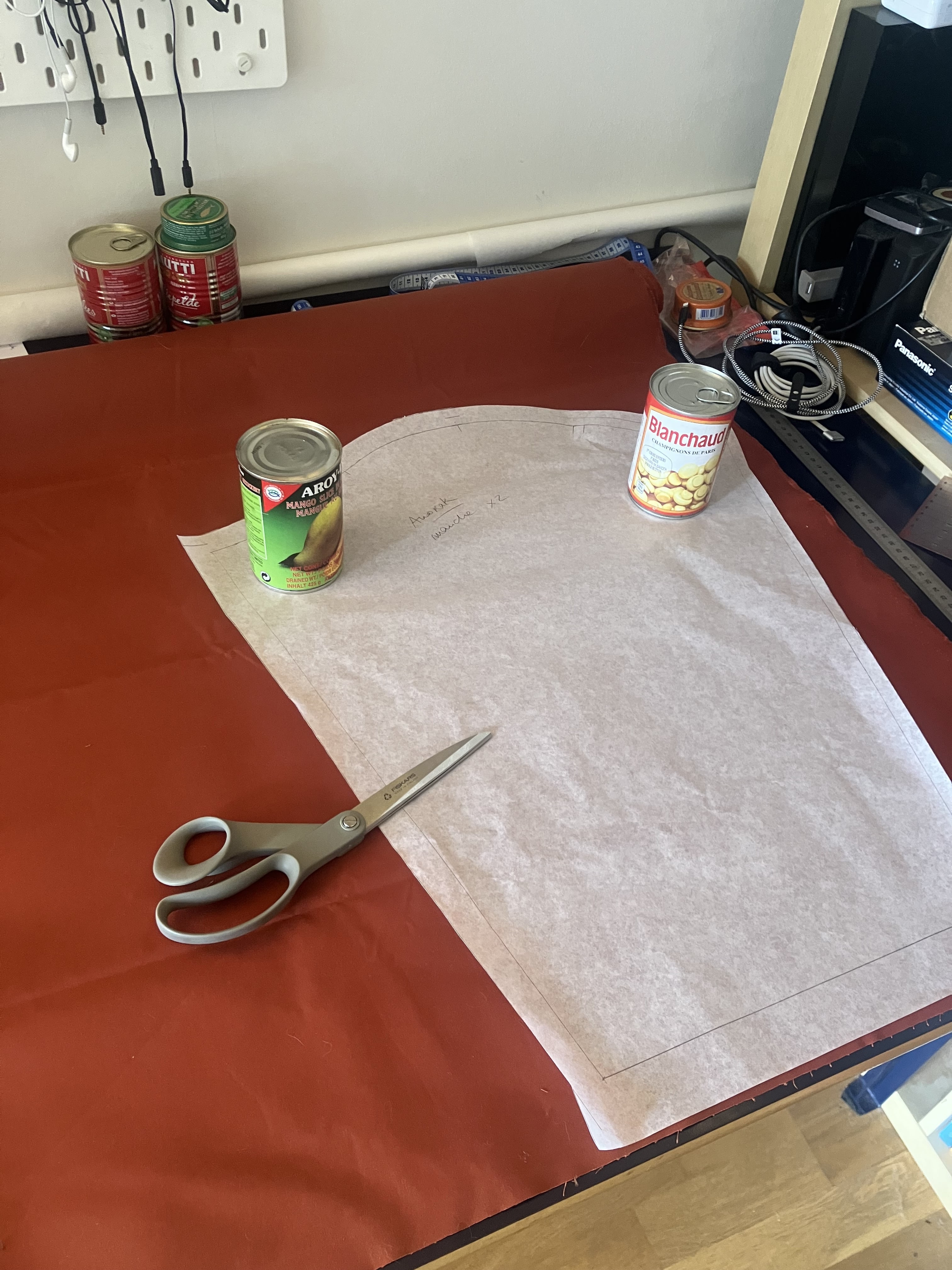 photo d’une table sur laquelle est posé un métrage de tissu avec un patron prêt à être découpé. le patron est tenu par des boîtes de conserve.
