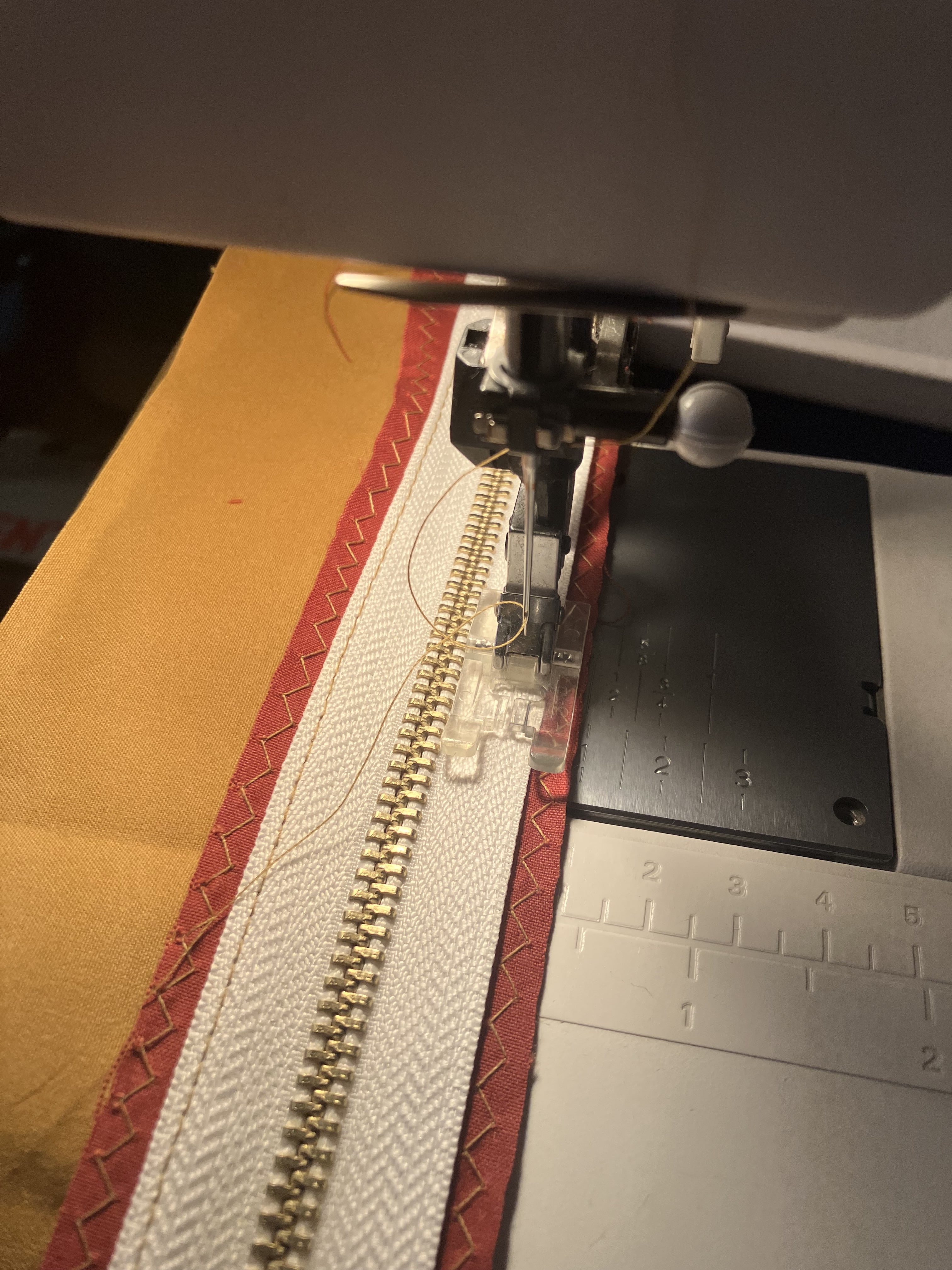 détail du pied d’une machine à coudre qui coud une fermeture éclair métallique à du tissu orange rouille