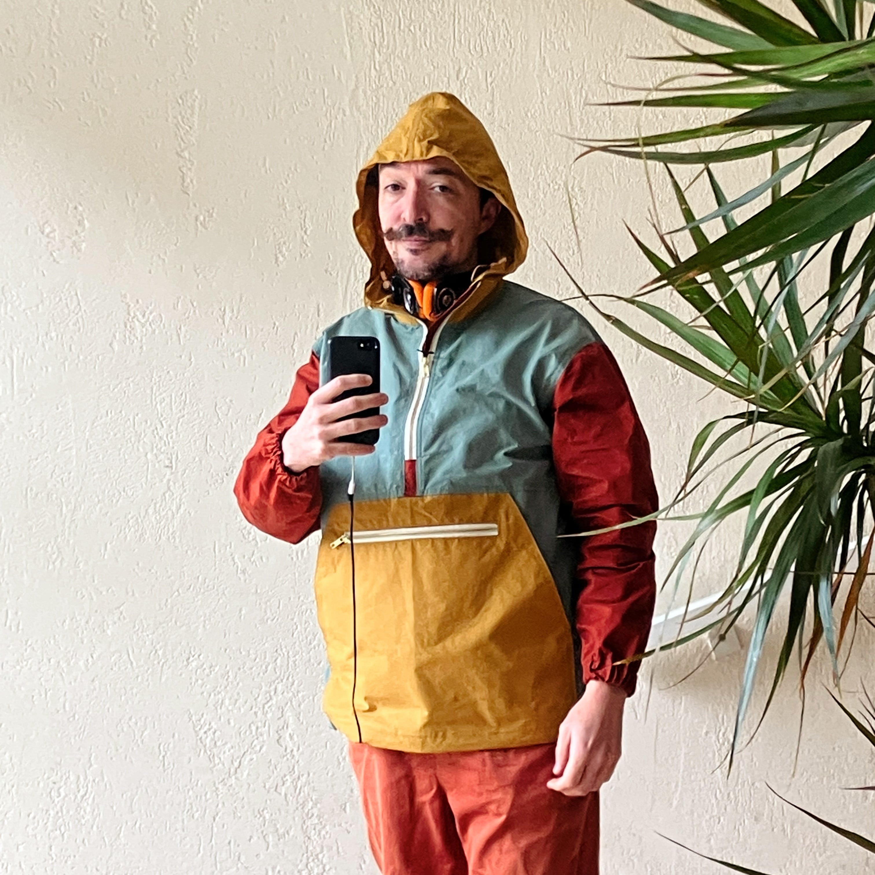 selfie dans un miroir d’un homme qui porte un anorak de trois couleurs, jaune cumin, orange rouille et vert tempête