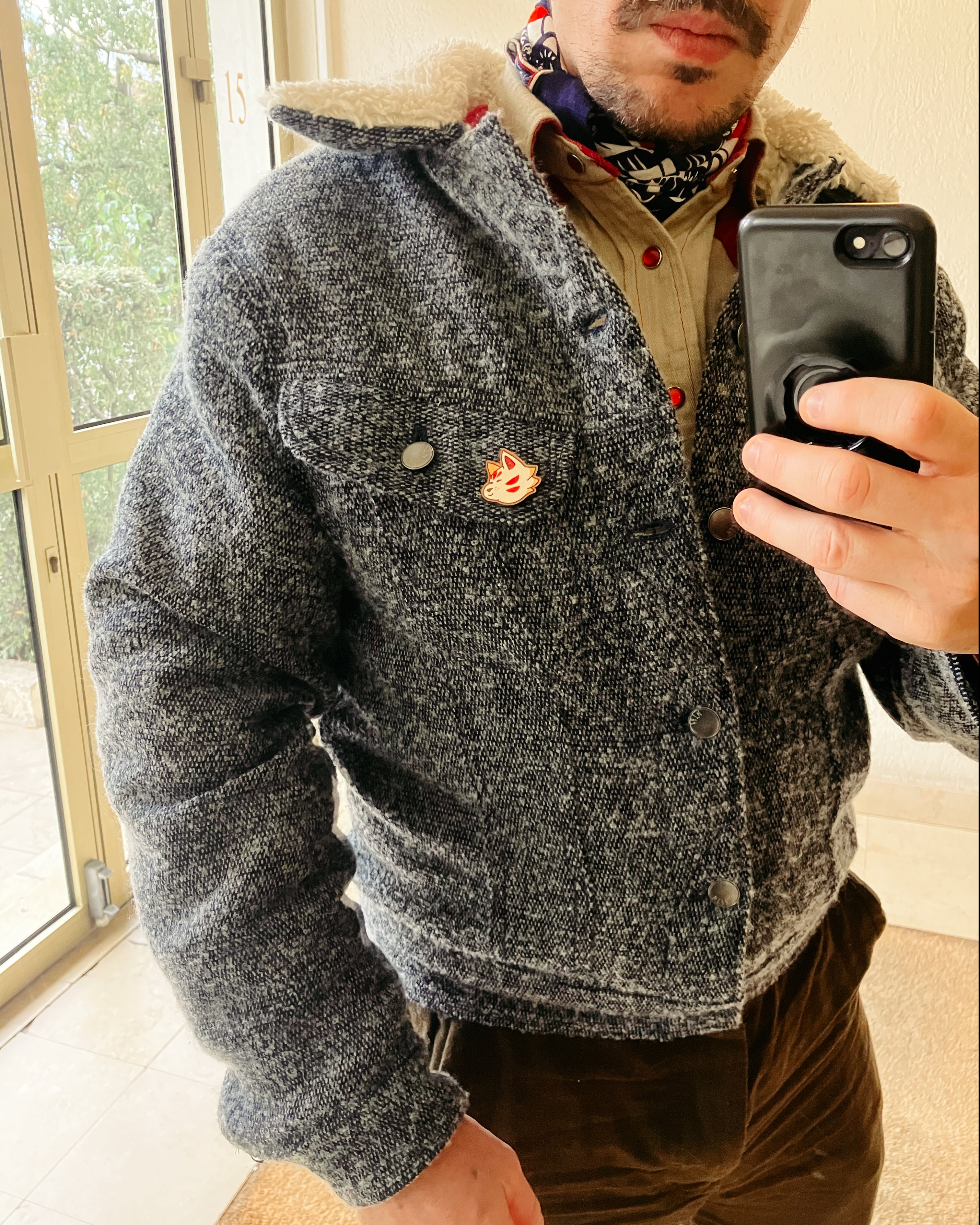 Détail du blouson porté par le même homme, le col a l’air tout doux, il a un pins sur le rabat de la poche de poitrine