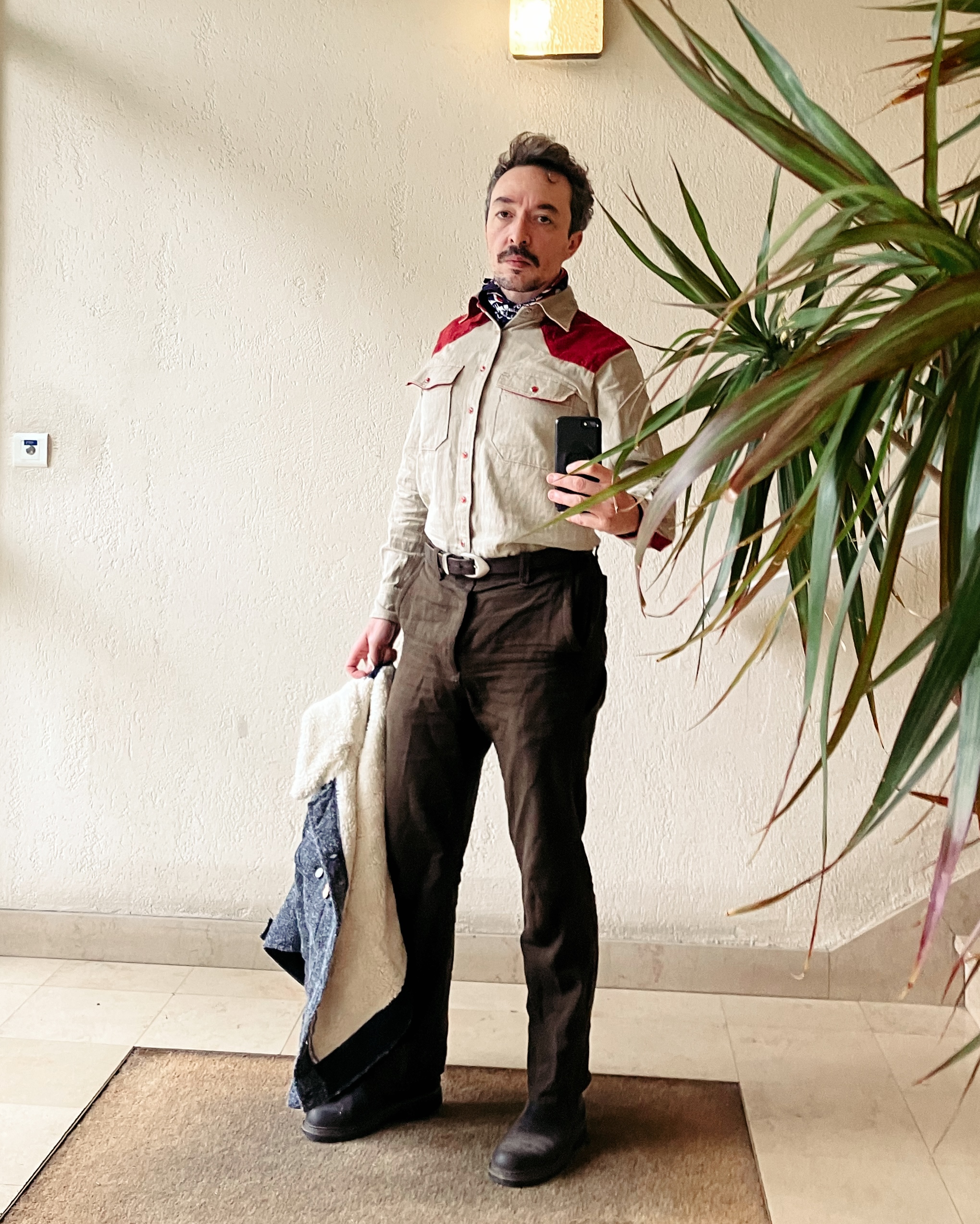 Photo du même homme sans son blouson. Il porte une chemise beige façon western avec des renforts d’épaule rouge et des boutons pression rouge.