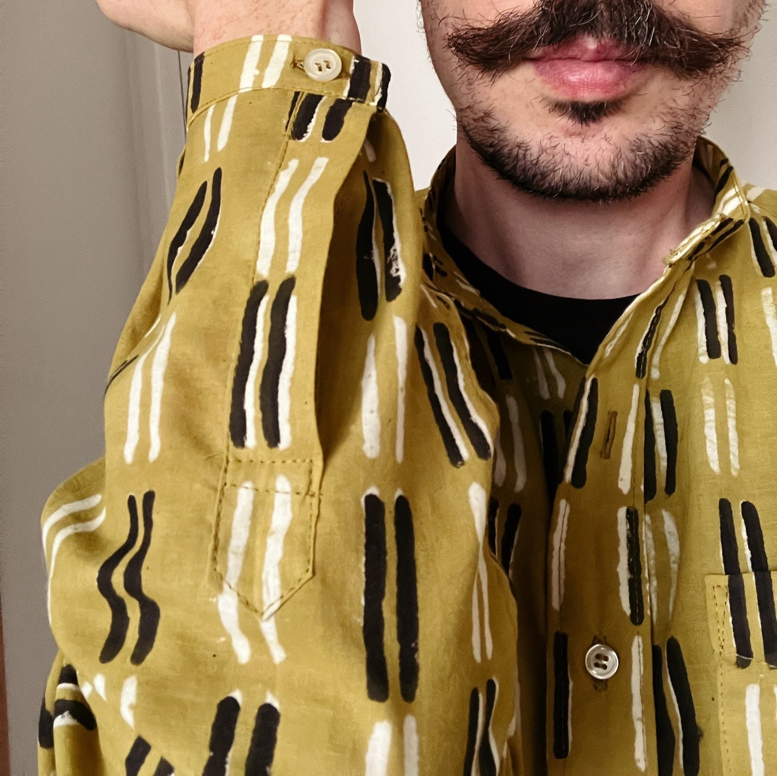 Selfie d’un homme qui montre le détail de la manche d’une chemise vert olive à motifs blancs et noirs