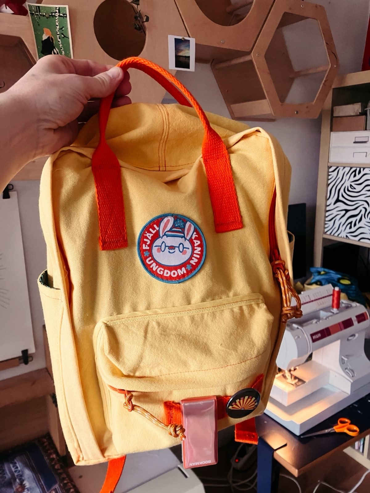 photo d’une main qui tient un sac jaune à bretelles oranges et écusson de lapin.