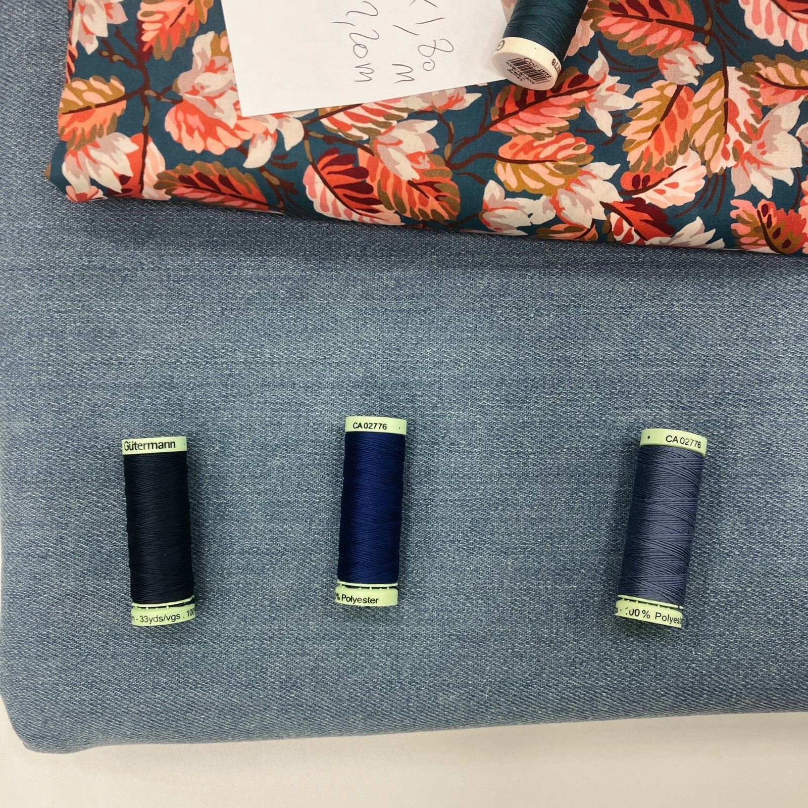 photo d’ambiance, un tissu à motif de feuilles d’automne, du denim bleu clair, et des fils à coudre de diverses teintes de bleu
